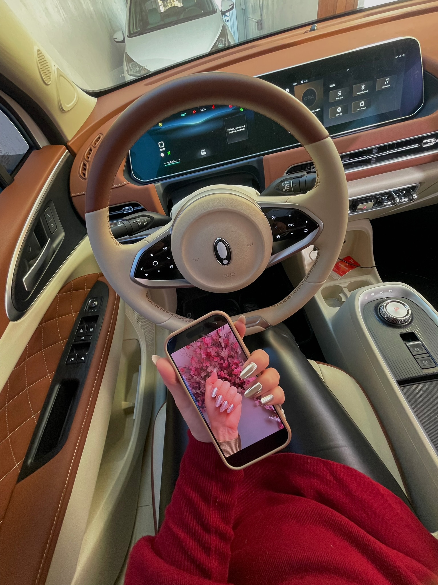 Mão com unhas cromadas segurando o celular dentro do carro